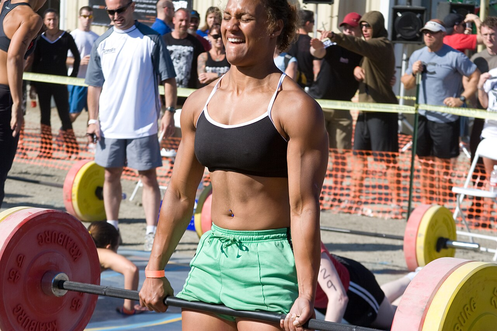 Fit woman executing a heavy barbell deadlift at an outdoor fitness event, highlighting glute and hamstring engagement.